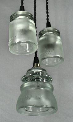 three glass jars are hanging from the ceiling with black cords in front of white background