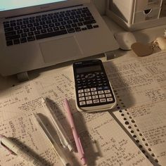 an open laptop computer sitting on top of a desk next to two pens and a calculator