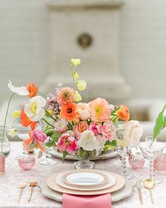 an arrangement of flowers on a table with plates and utensils in the foreground