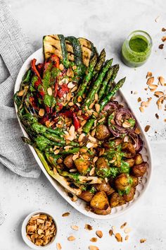 a white platter filled with asparagus, potatoes and almonds next to a jar of green pesto dressing