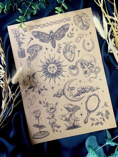 a sheet of paper with tattoos on it next to some plants and flowers, including feathers