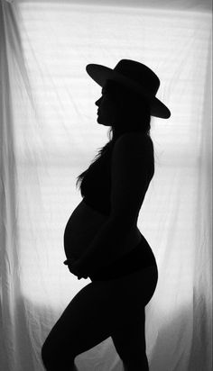 a pregnant woman wearing a cowboy hat poses in front of a curtain