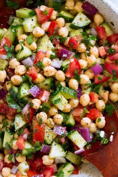 a salad with chickpeas, cucumber and tomatoes in a white bowl