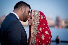 a bride and groom standing next to each other in front of the water at sunset