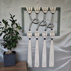 a wall hanging with tassels on it next to a potted plant