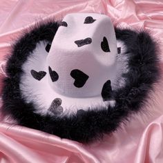 a black and white hat with hearts on it sitting on a pink satin material background