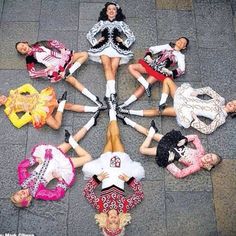 six women in colorful outfits are sitting on the ground and one is holding her hands together