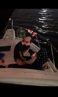 two people sitting on a boat in the water at night with an american flag flying above them