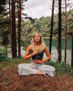 a woman sitting in the middle of a forest doing yoga