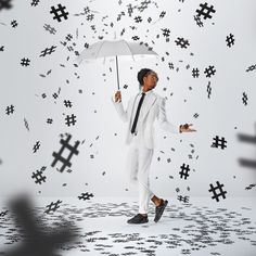 a man in a white suit and tie holding an umbrella over his head while surrounded by black crosses