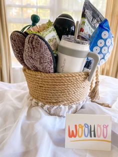 a basket filled with items sitting on top of a bed next to a sign that says woohoo