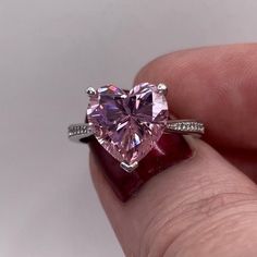 a pink heart shaped diamond ring on someone's finger