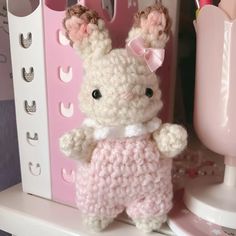 a crocheted bunny is standing next to a pink vase and toothbrush holder