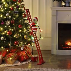 a christmas tree with presents under it and a ladder next to it that is lit up