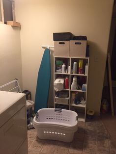 a laundry basket sitting in the middle of a kitchen floor next to a shelf filled with toiletries