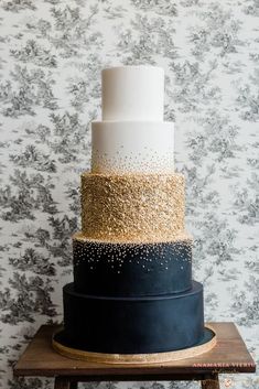 a three tiered cake with black, white and gold frosting on a wooden stand