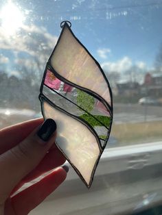 a hand holding up a stained glass piece that is shaped like a leaf and has grass in it