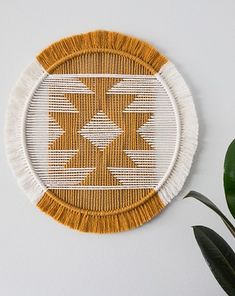 a white and yellow wall hanging on the wall next to a green potted plant