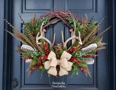 a wreath with deer antlers, berries and pine cones is hanging on the front door