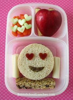 a lunch box with an apple, carrots and crackers in the shape of a smiley face