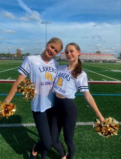 two cheerleaders pose for a photo on the football field