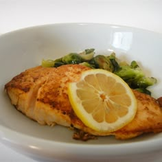 a white bowl filled with chicken, broccoli and lemon wedges on top of it