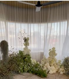 an arrangement of white flowers and greenery in front of a sheer curtained window