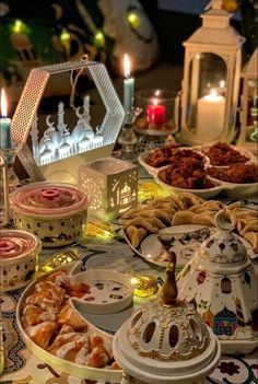 a table topped with lots of different types of food next to lit candles and teapots