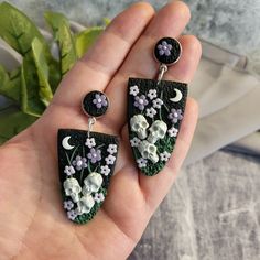 a pair of earrings with flowers and moon in the middle on a person's hand