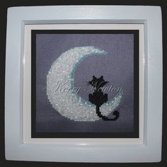 a cross stitch picture of a cat sitting on the moon with it's tail hanging down