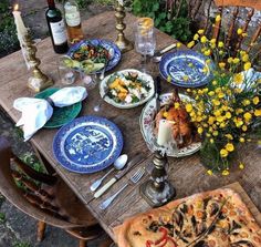 a wooden table topped with blue and white plates covered in food next to yellow flowers