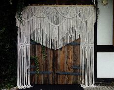 a wooden door decorated with white macrame hanging from it's side and surrounded by greenery