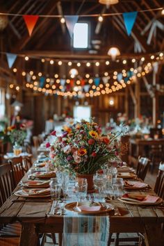 a wooden table topped with plates and vases filled with flowers next to hanging lights