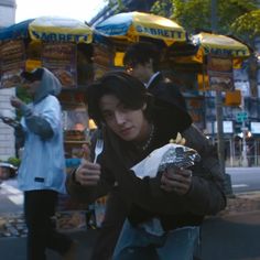 a man is eating something while standing on the side walk in front of some food stands