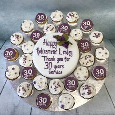 a birthday cake decorated with white frosting and purple icing, surrounded by 30 cupcakes