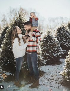 a man and woman holding a baby in their arms while standing next to a christmas tree