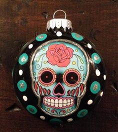 a glass ornament with a skull and rose painted on the front, sitting on a wooden surface