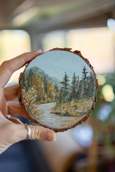 a person holding up a piece of wood with an image of a river on it