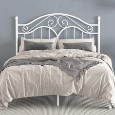 a white metal bed with two pillows and blankets on it, against a blue wall