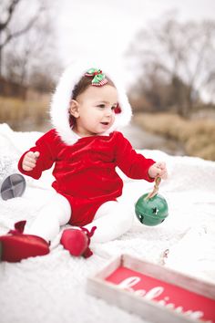 a baby sitting on the ground wearing a santa hat and holding a green teapot