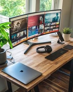 a wooden desk with two computer monitors and a laptop on it, in front of a window