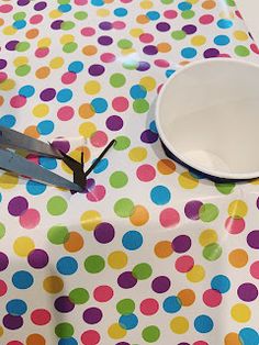 a pair of scissors cutting through the center of a polka dot table cloth with white bowl on top