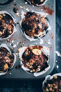 chocolate muffins with nuts and other toppings in a muffin tin on a table