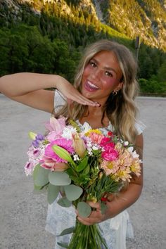 a woman holding a bouquet of flowers in front of her face with mountains in the background