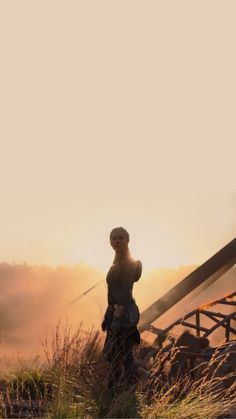 a woman standing on top of a grass covered field next to a wooden structure in the distance