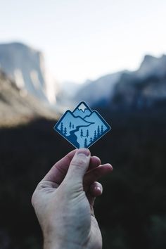 a hand holding up a sticker with mountains and trees in the backgroud