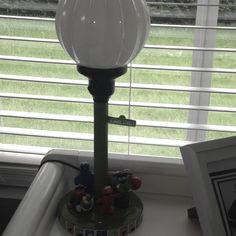 a lamp sitting on top of a table next to a window with blinds behind it