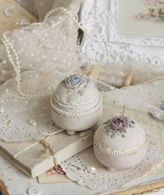 two small white boxes sitting on top of a table next to lace doily and pearls