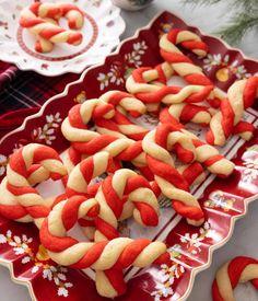 some red and white cookies are on a plate with candy canes in the shape of pretzels