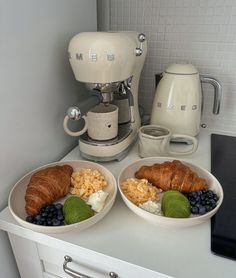 two white bowls filled with breakfast foods next to a coffee maker on a counter top